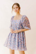 Woman wearing a purple paint stroke print dress against a plain background