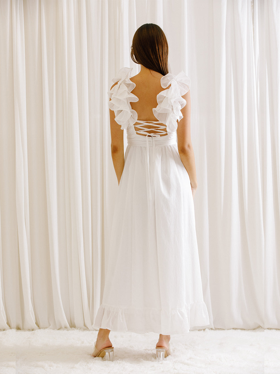 Back view of a woman wearing a white dress standing in front of white curtains