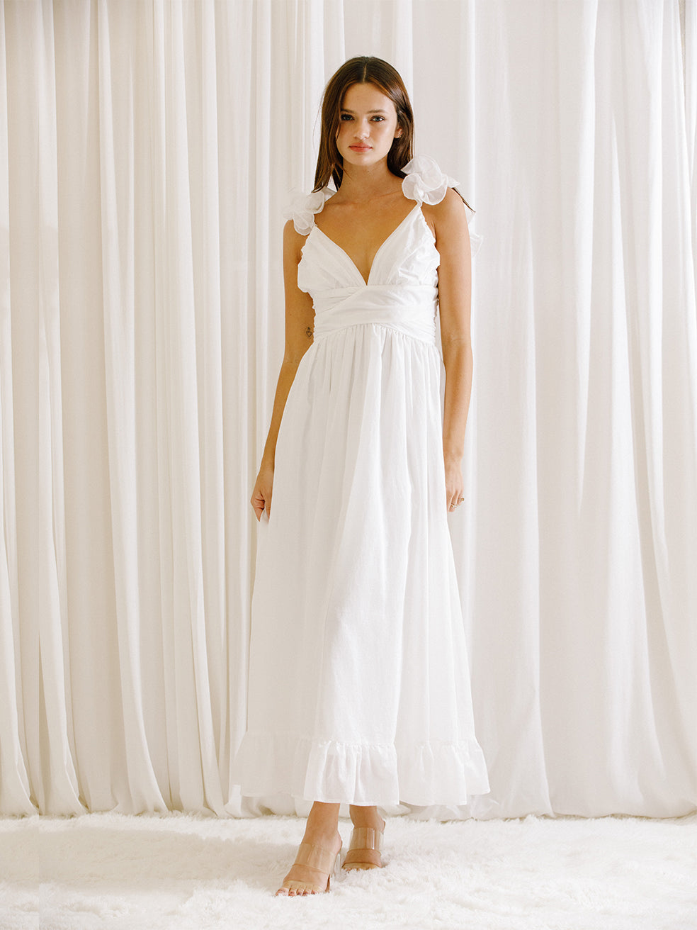 Woman wearing a white dress standing in front of white curtains