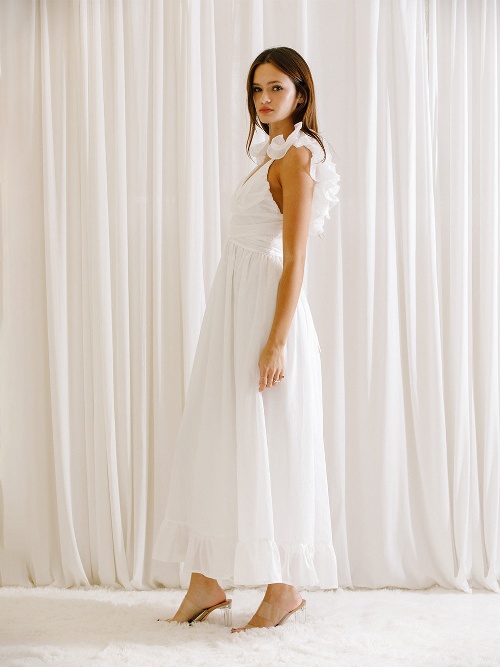 Side view of a woman wearing a white dress standing in front of white curtains