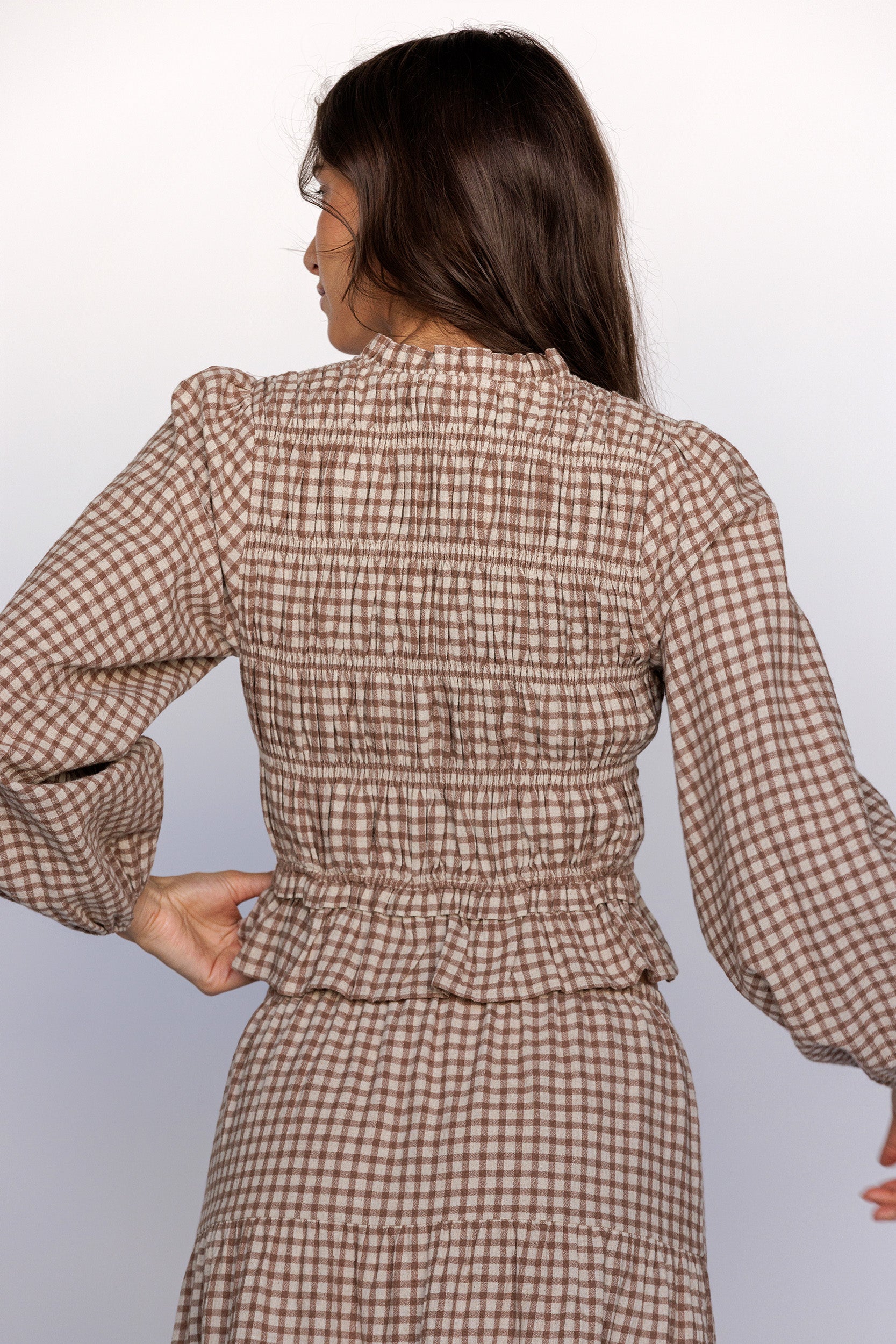Back view of a woman wearing a brown checkered outfit against a white background