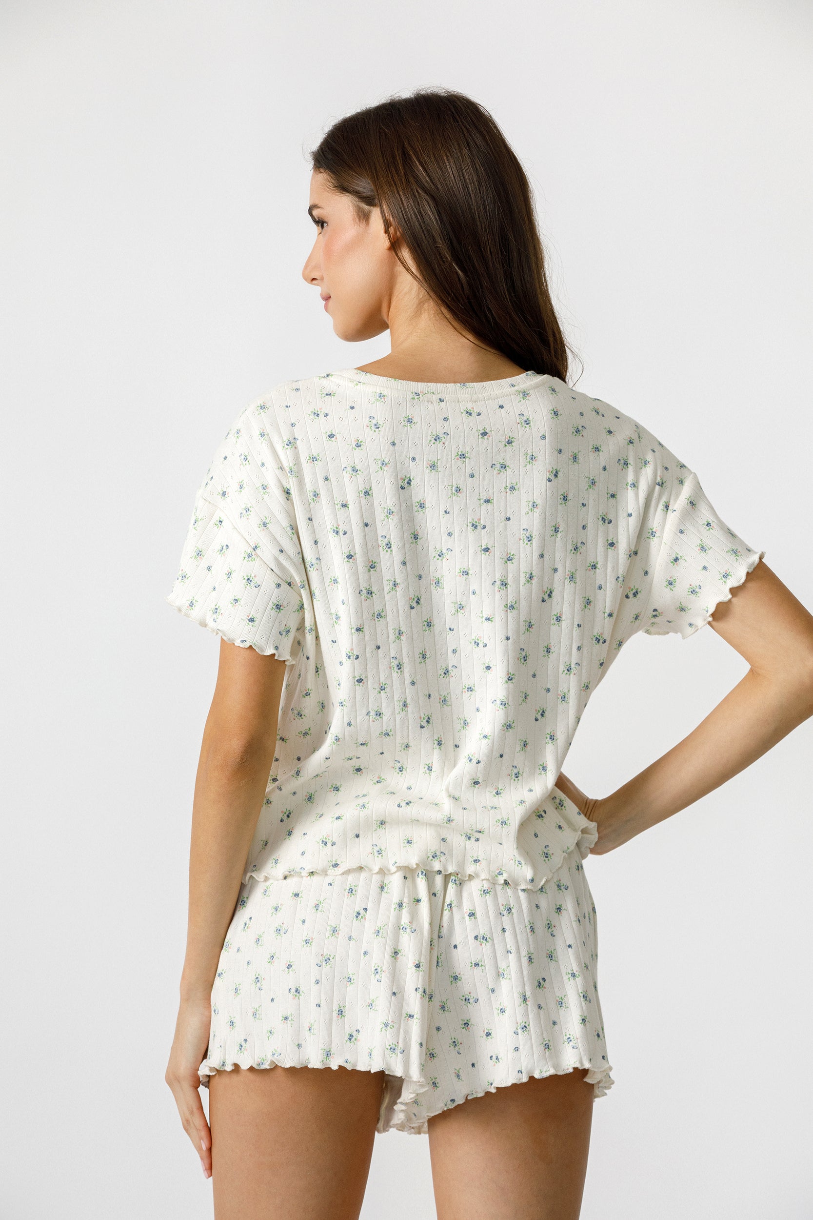 Back view of a woman wearing a cream blue floral pajama set on a plain background