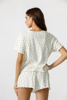 Back view of a woman wearing a cream blue floral pajama set on a plain background