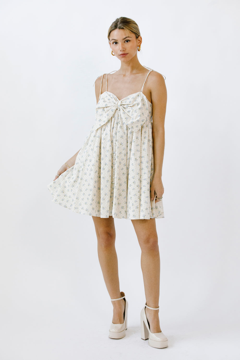 Woman wearing a cream blue floral mini dress with a bow detail on a white background