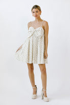 Woman wearing a cream blue floral mini dress with a bow detail on a white background