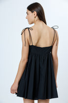Back view of a woman wearing a black dress with thin straps on a white background