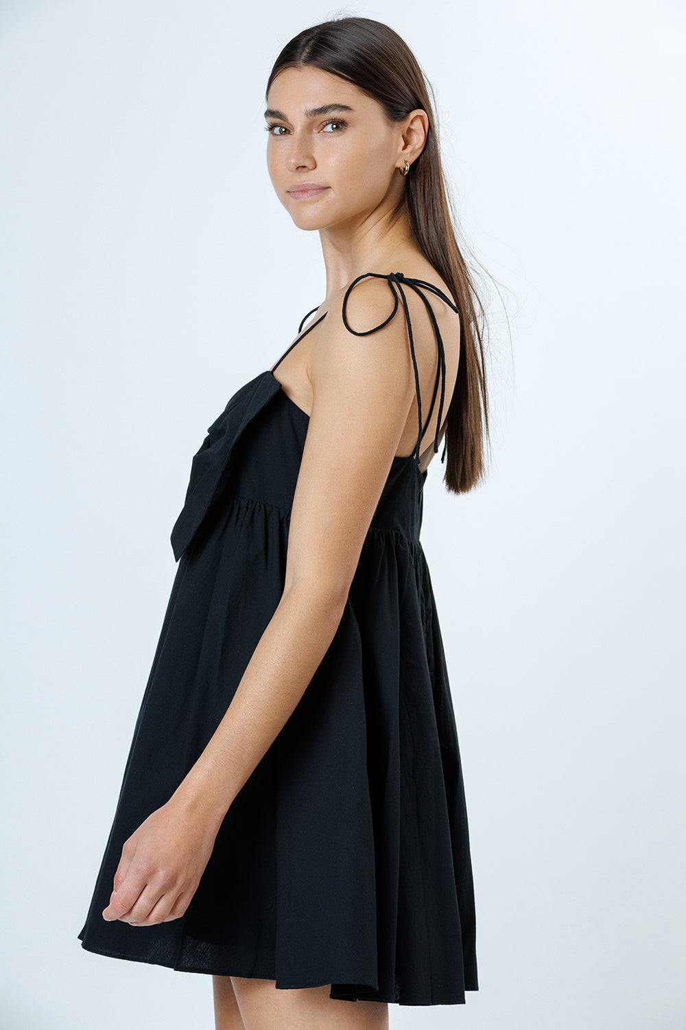 Side view of a woman wearing a black dress with thin straps on a white background