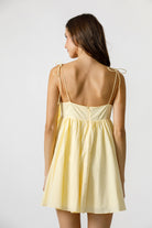 Back view of a woman wearing a light yellow dress with thin straps on a white background