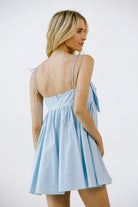 Back view of a woman wearing a light blue dress with thin straps on a white background