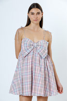 Woman wearing a pink plaid dress with a bow detail on a white background