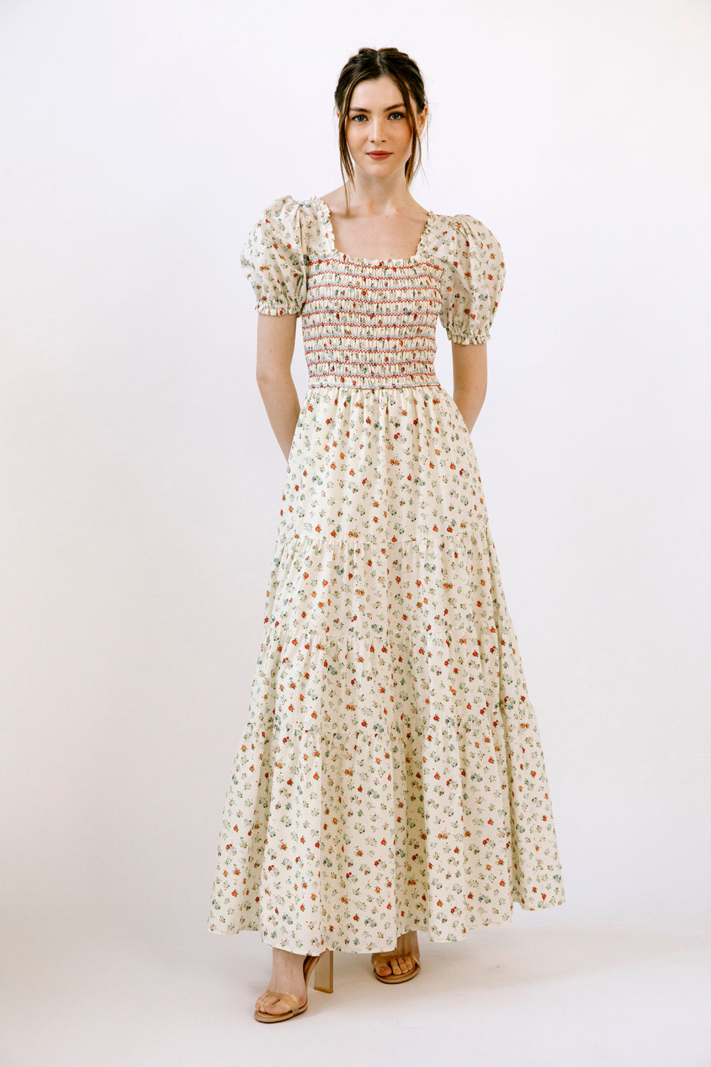 Woman wearing a floral maxi dress and beige heels on a white background