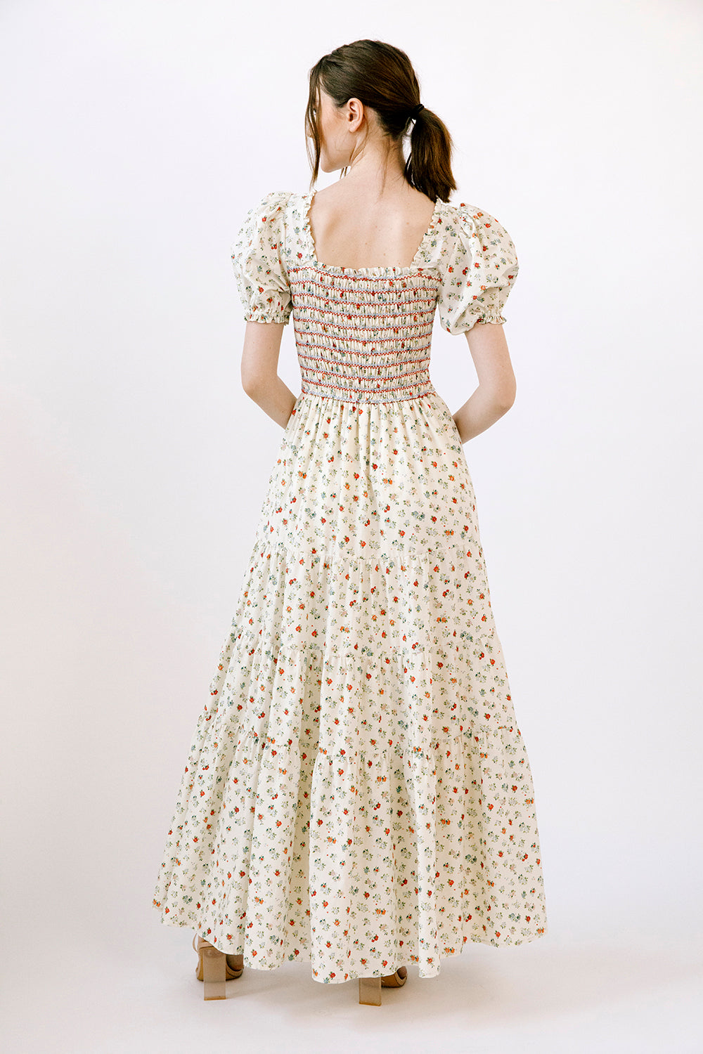 Back view of a woman wearing a cream and red floral dress on a white background