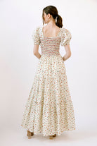 Back view of a woman wearing a cream and red floral dress on a white background