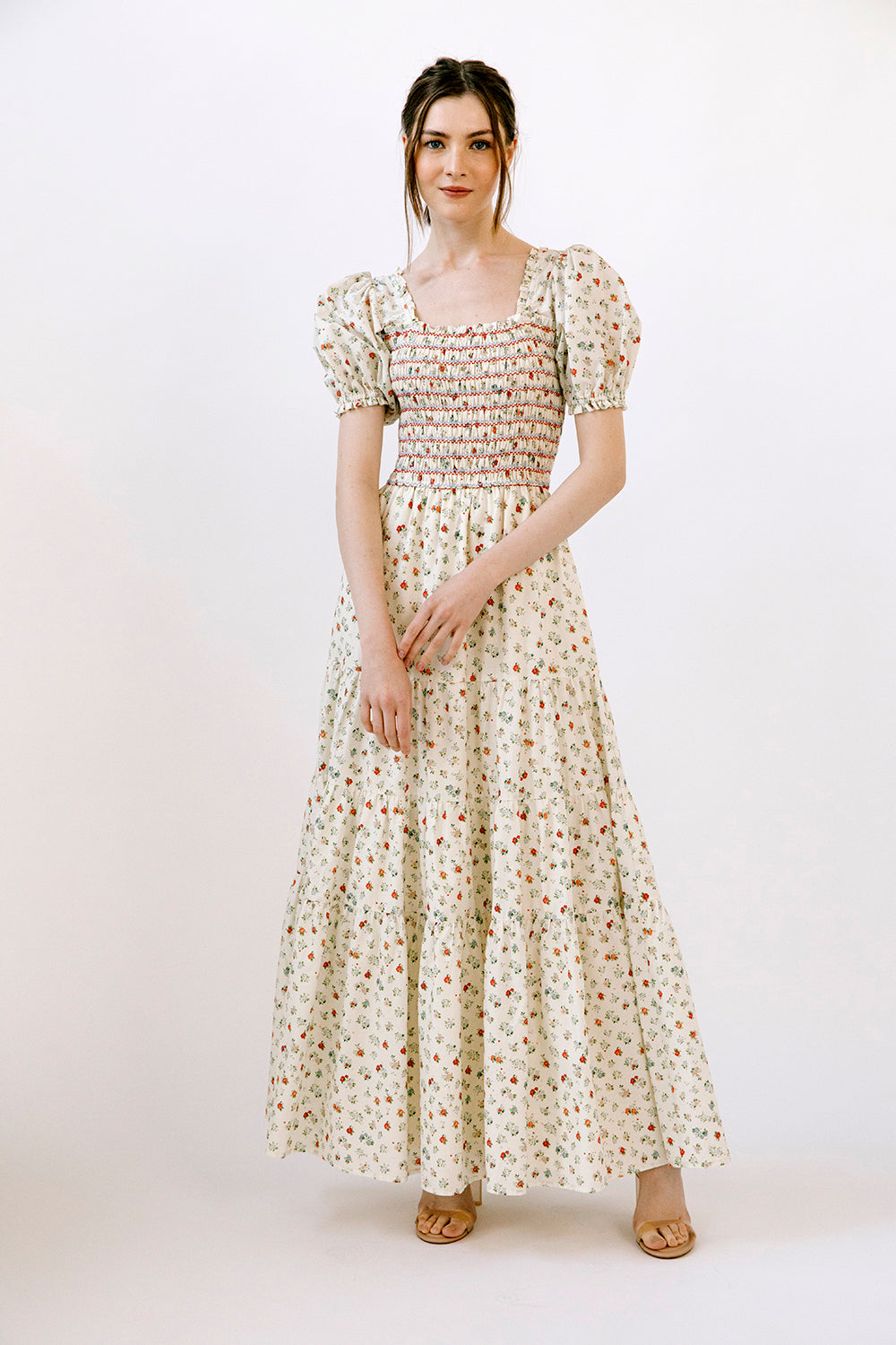 Woman wearing a cream and red floral maxi dress on a white background
