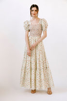 Woman wearing a cream and red floral maxi dress on a white background