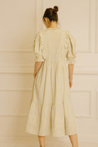 Back view of a woman wearing a light-colored dress with floral pattern against a neutral wall.