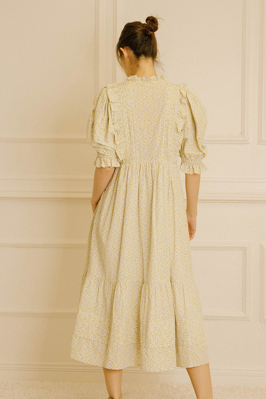 Back view of a woman wearing a light-colored dress with floral pattern against a neutral wall.