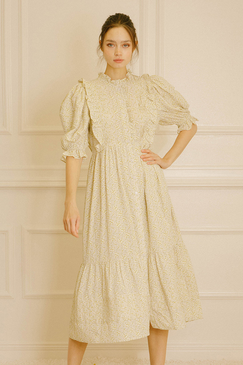 Woman wearing a light-colored dress with floral pattern against a neutral wall.