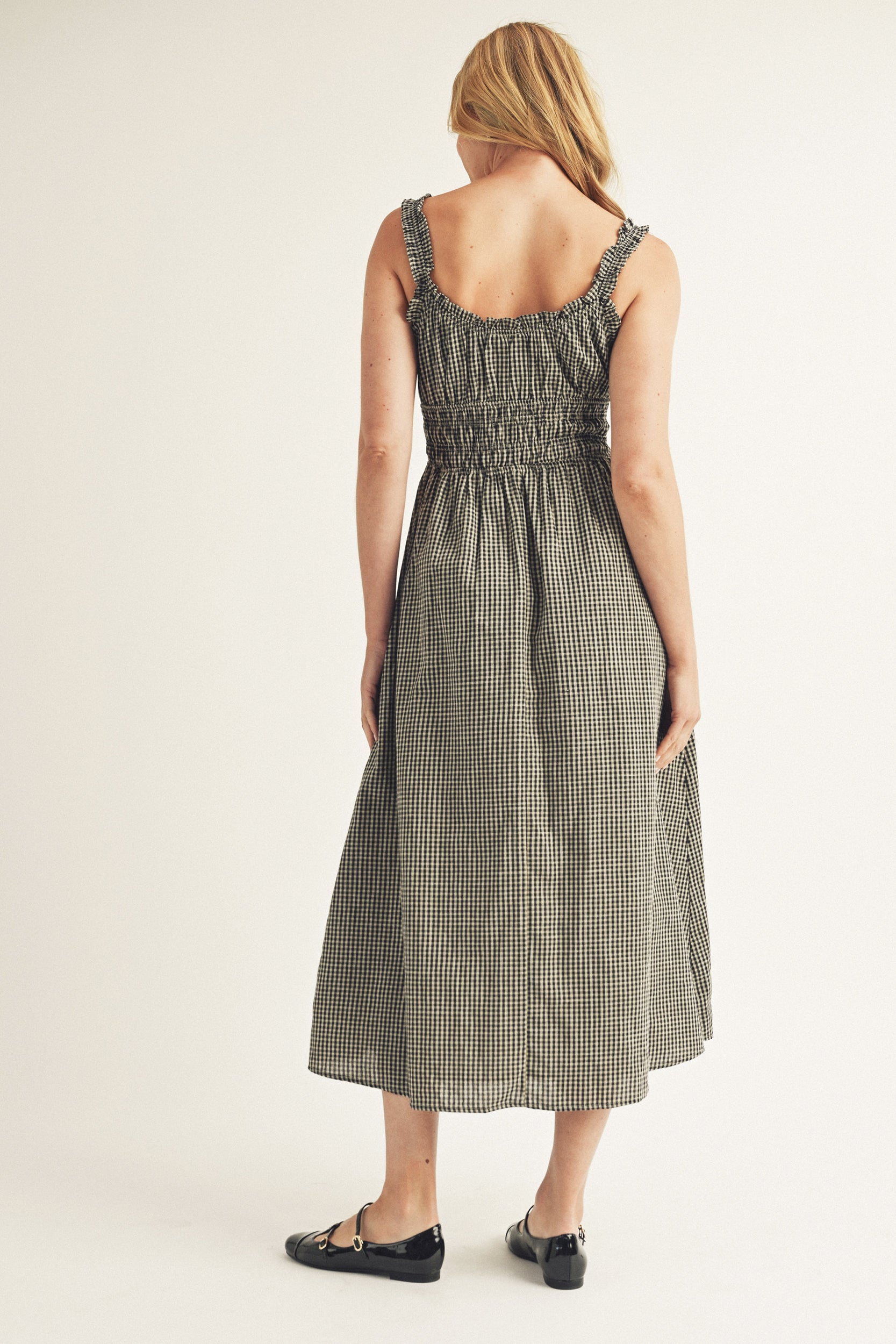 Back view of a woman wearing a checkered dress on a plain background