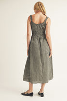 Back view of a woman wearing a checkered dress on a plain background