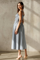 Side view of a woman wearing a blue checkered dress against a neutral background