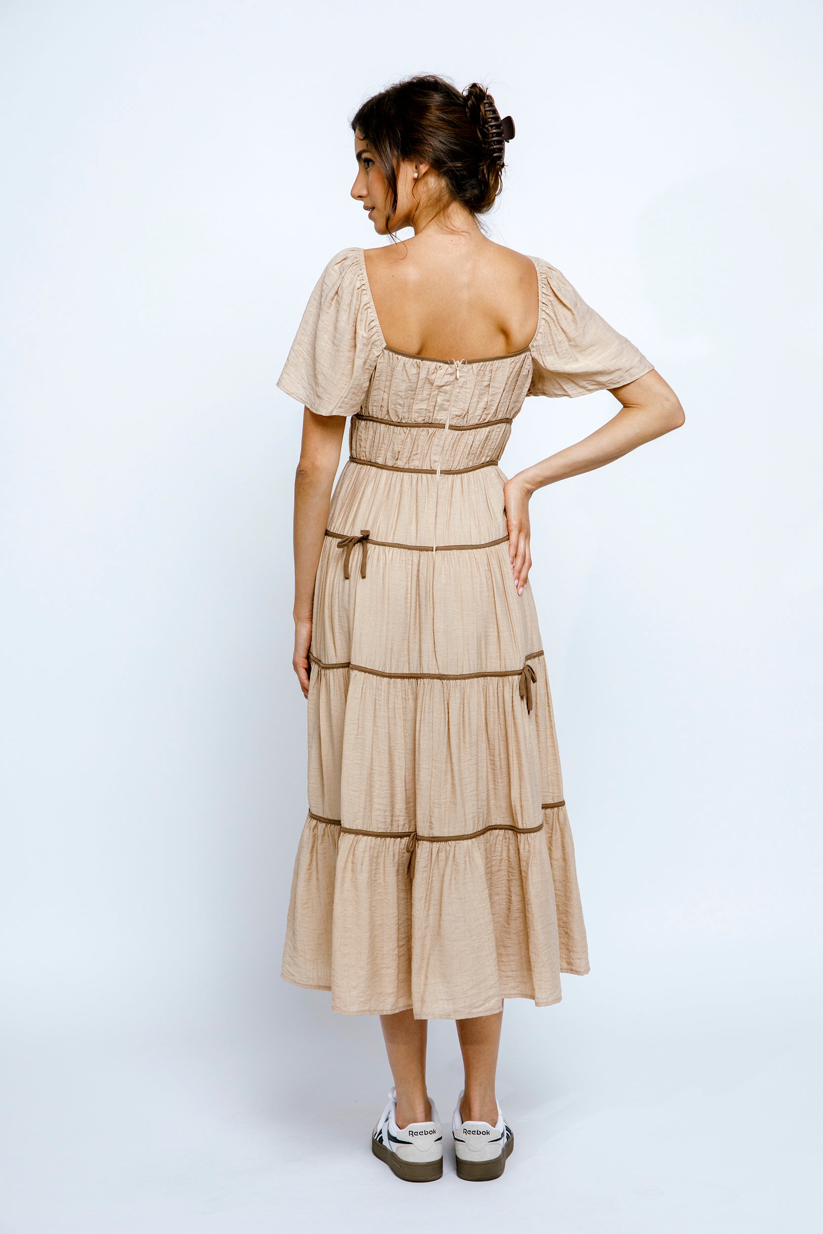 Back view of a woman wearing a beige dress with a layered skirt on a white background