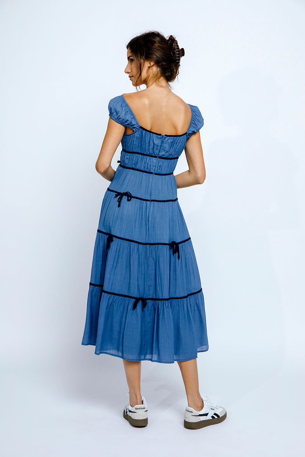 Back view of a woman wearing a blue dress with navy accents on a white background
