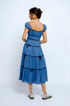 Back view of a woman wearing a blue dress with navy accents on a white background