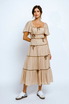 Woman wearing a beige dress with tiered layers on a white background