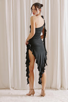 Woman wearing a black one-shoulder dress with ruffles and beige shoes