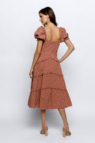 Back view of a woman wearing a mauve floral dress on a white background