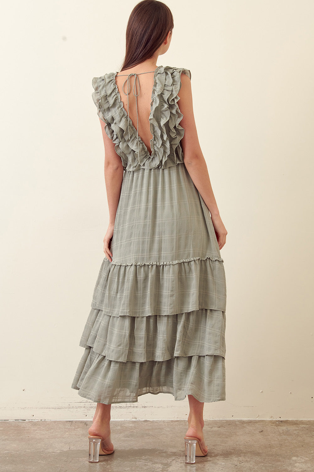 Back view of a woman wearing a green tiered dress against a plain background