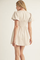 Woman wearing a beige dress with puffed sleeves on a plain background