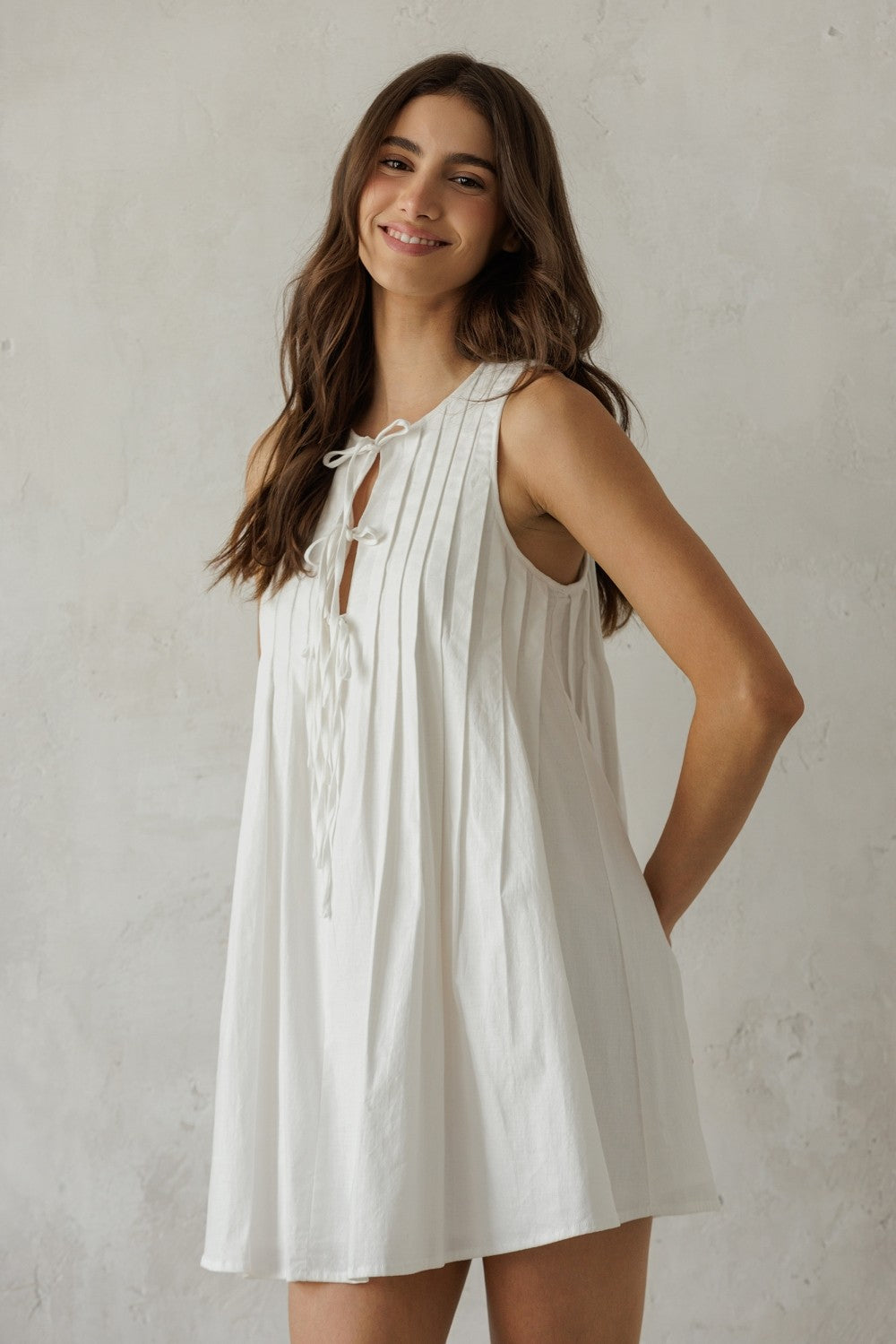 Woman wearing a white sleeveless dress with a pleated design against a plain background