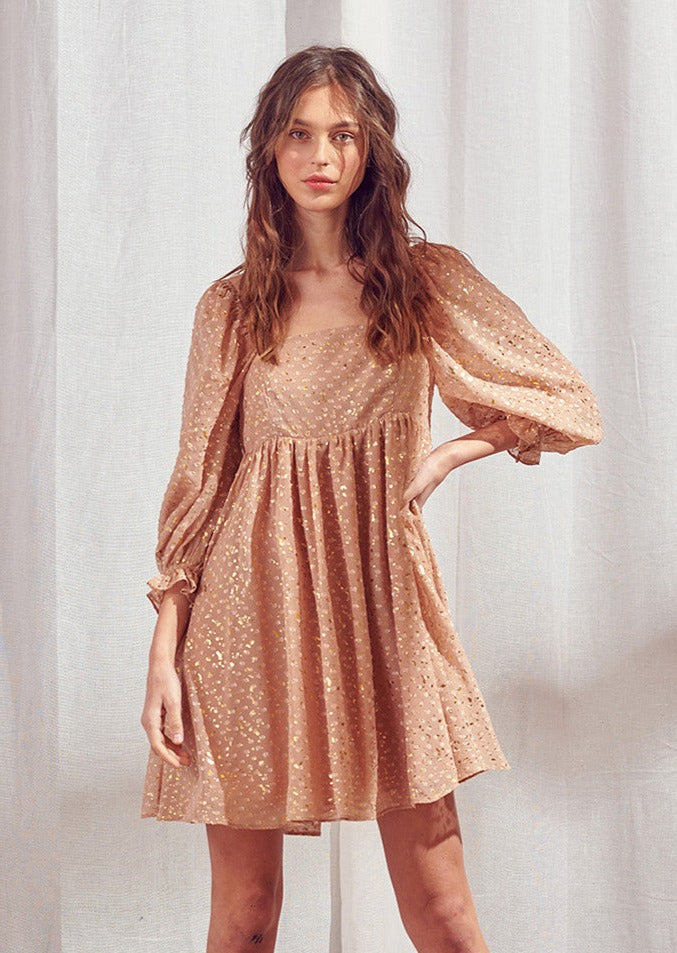 Woman wearing a brown dress with shimmering gold flaked embroidered dots against a white curtain background