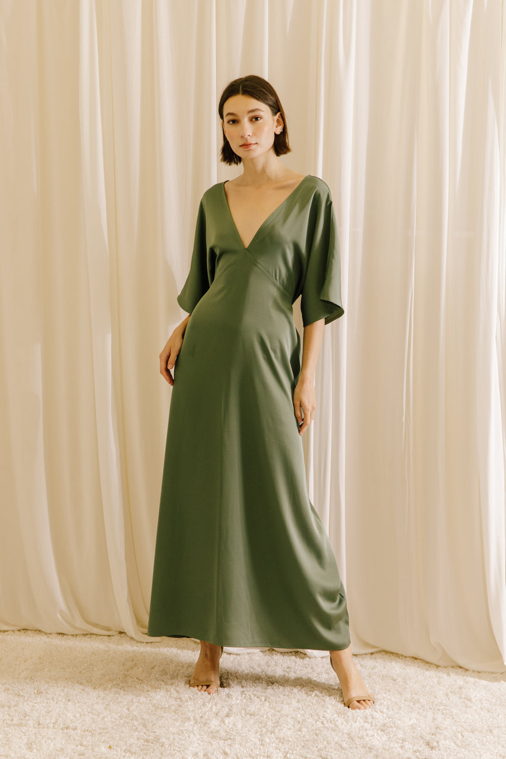 Woman wearing an olive green V-neck maxi dress with short sleeves and fluid drape