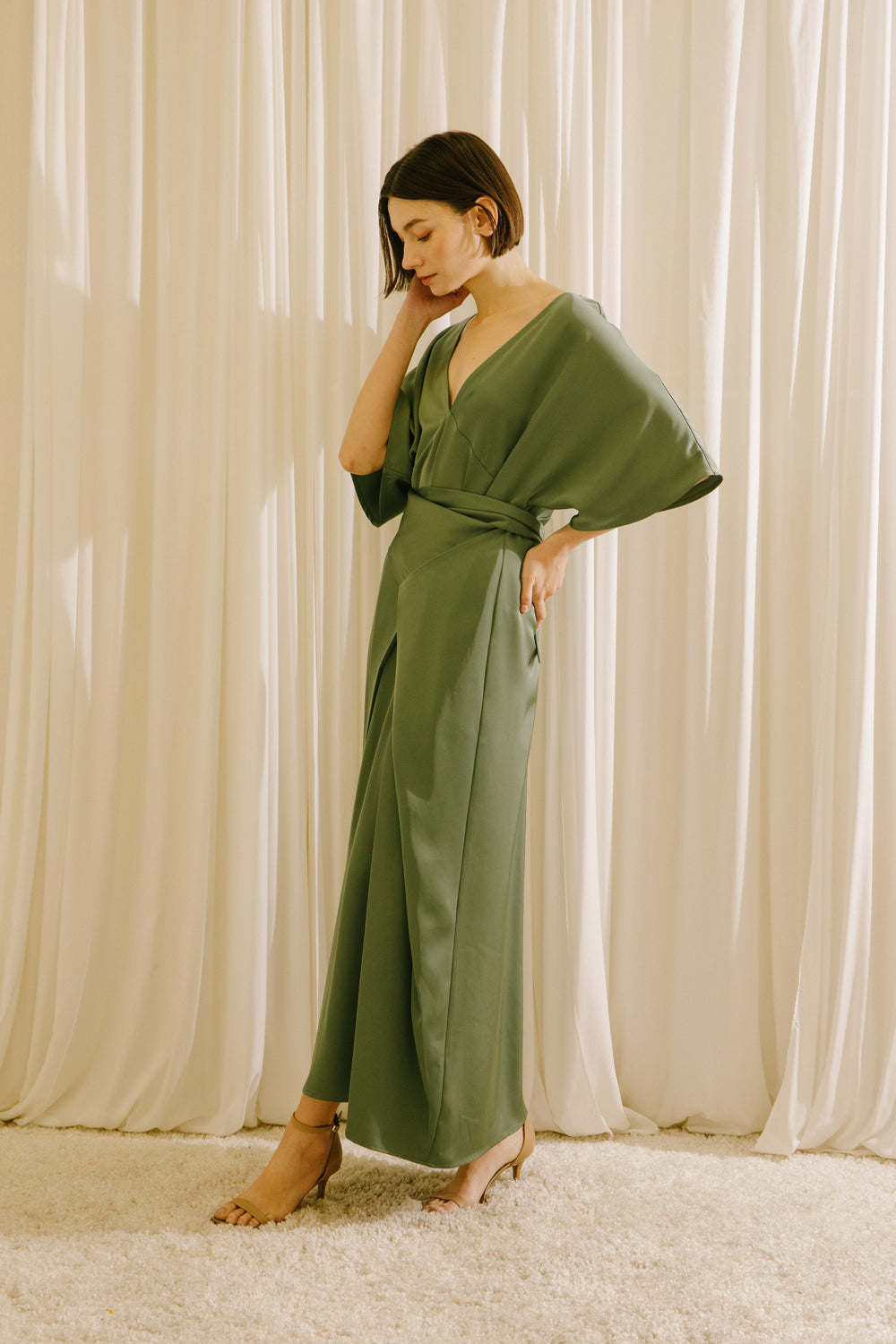 Side view of a woman wearing an olive green V-neck maxi dress with short sleeves and fluid drape