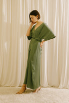 Side view of a woman wearing an olive green V-neck maxi dress with short sleeves and fluid drape