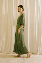 Side view of a woman wearing a green dress standing against a beige curtain backdrop