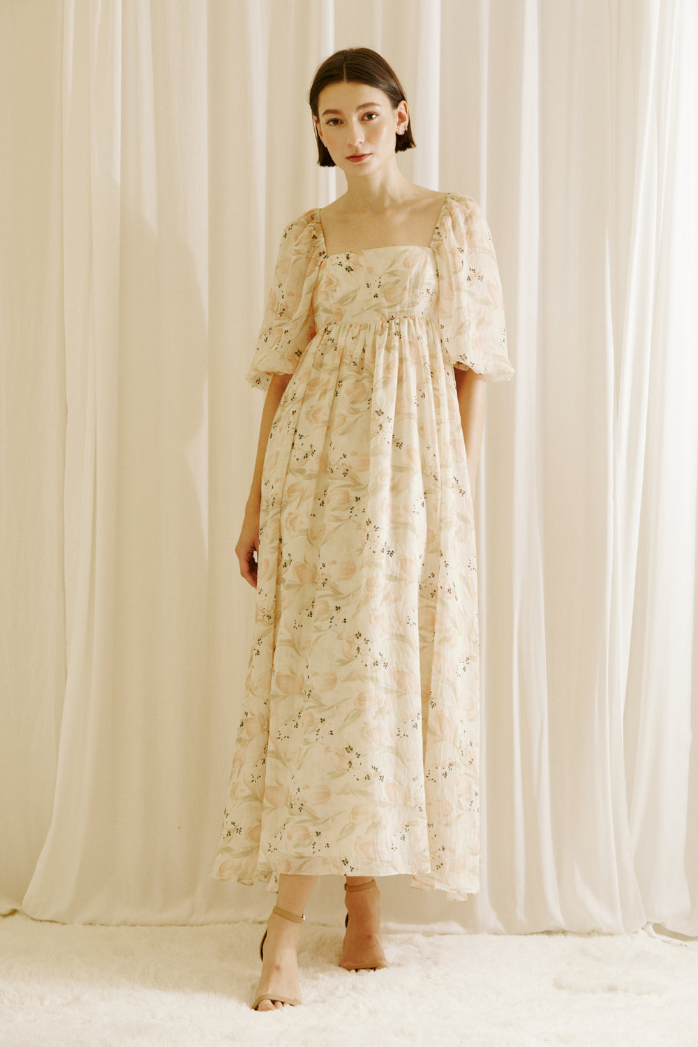Woman wearing a floral dress with tulips print standing against a white curtain backdrop