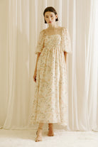 Woman wearing a floral dress with tulips print standing against a white curtain backdrop