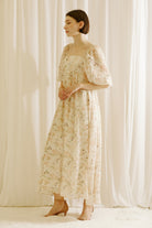 Side view of a model wearing a floral dress with a tulip print standing against a white curtain backdrop