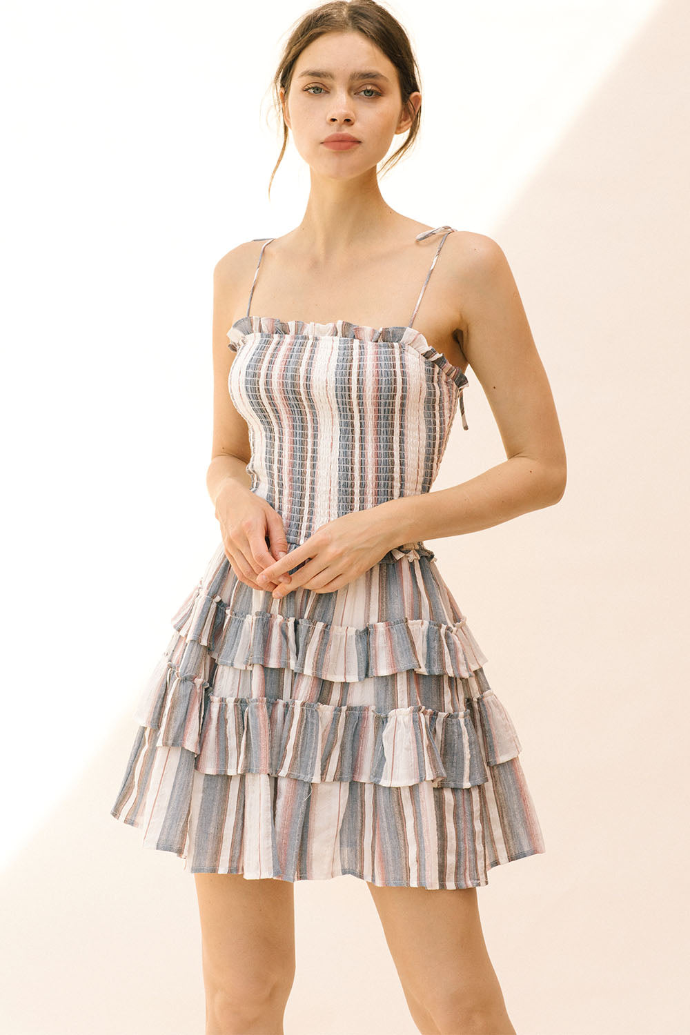 Woman wearing a gray and white tiered striped dress on a plain background