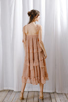 A woman viewed from behind wearing a rust floral midi dress with cascading ruffle layers, tassel tie straps, and a relaxed flowy fit.