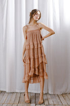 A model wearing a rust floral midi dress with cascading ruffle layers, tassel tie straps, and a relaxed flowy fit.