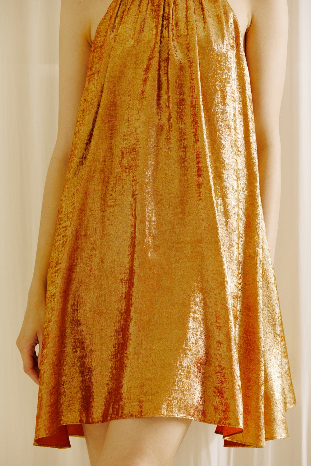 Bronze dress against a white curtain background