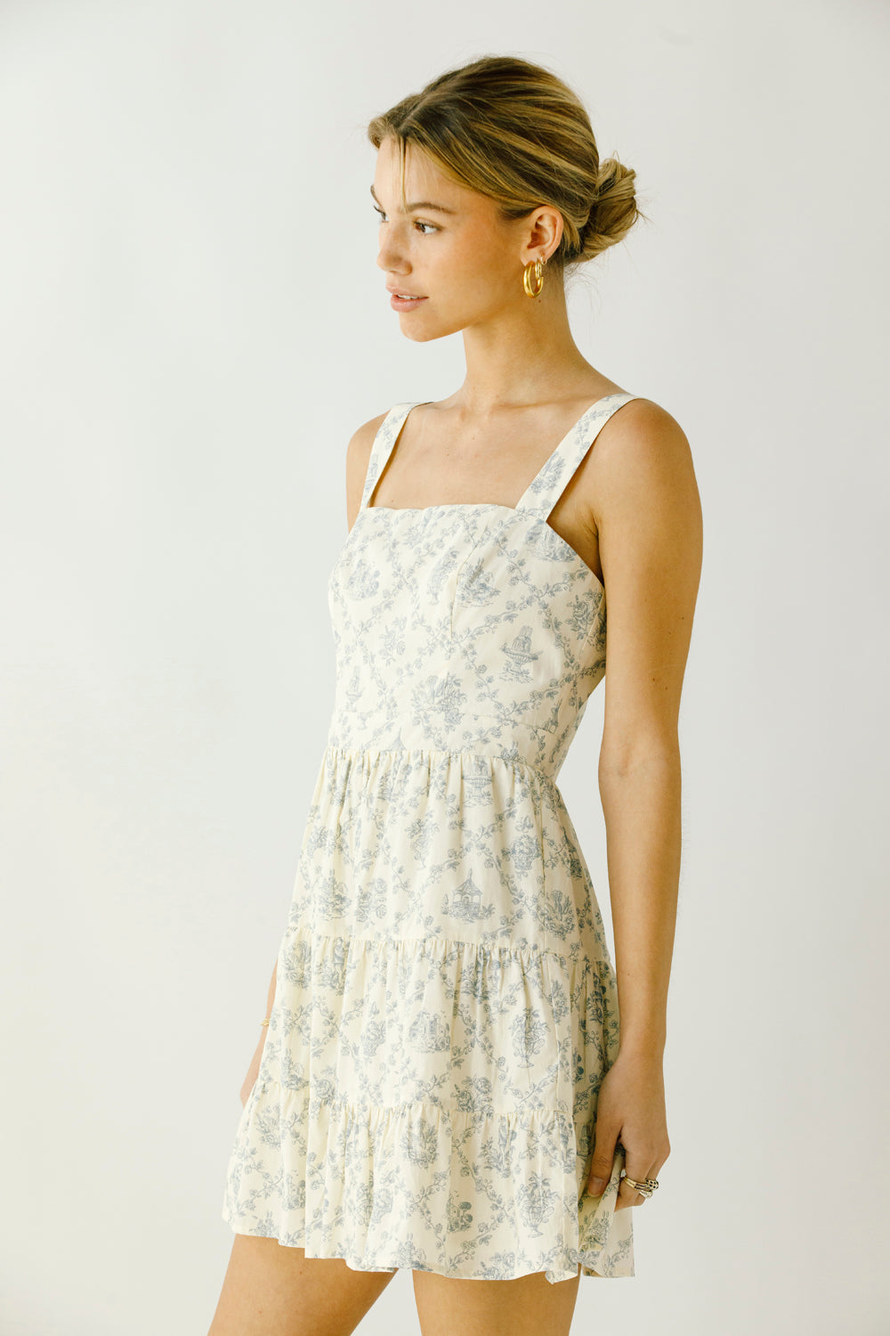 Side view of a woman wearing a cream floral dress against a plain background