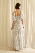 Back view of a woman wearing a floral dress standing in front of sheer curtains
