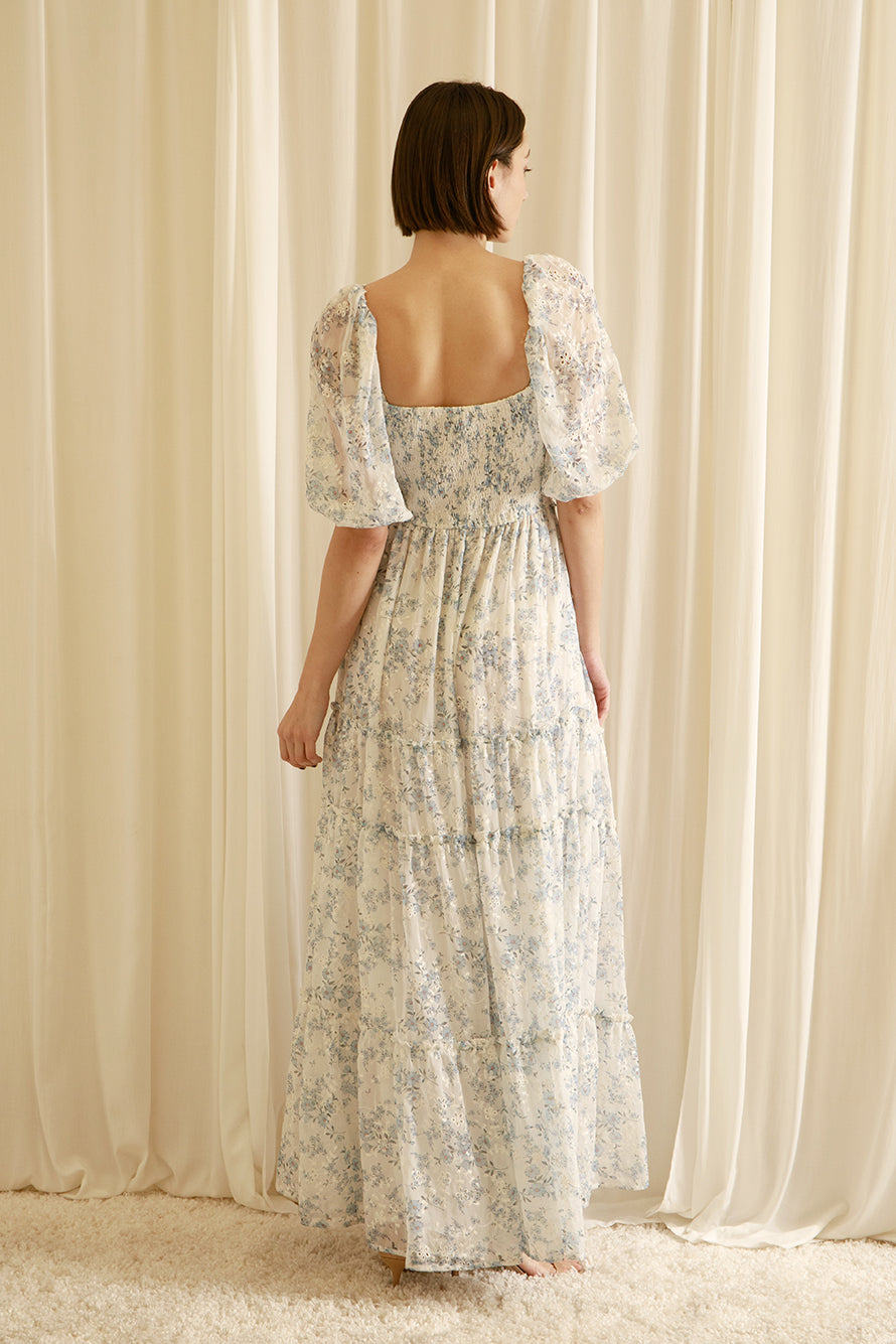 Back view of a woman wearing a floral dress standing in front of sheer curtains