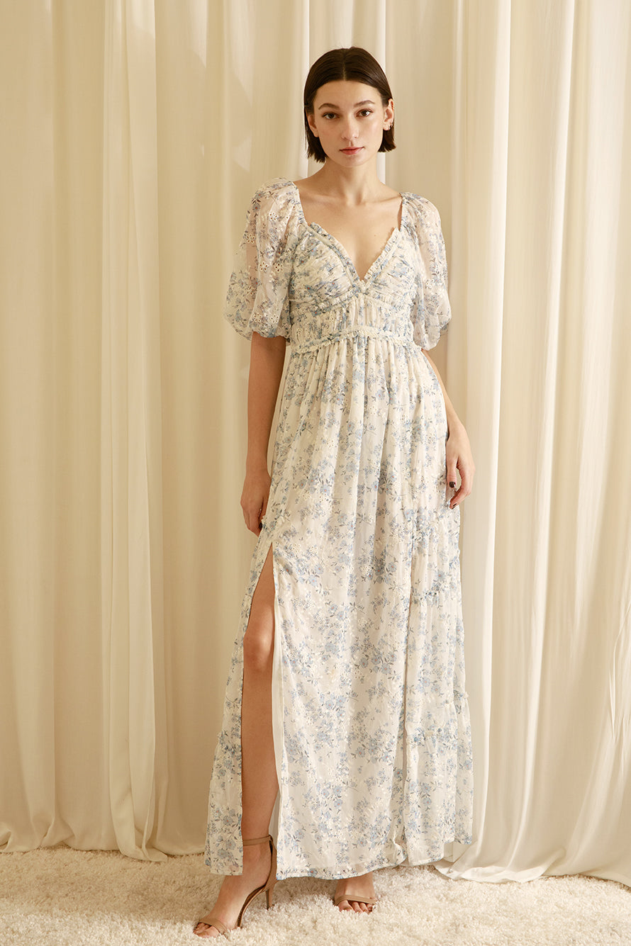 Woman wearing a floral dress with a slit in front against a beige curtain background